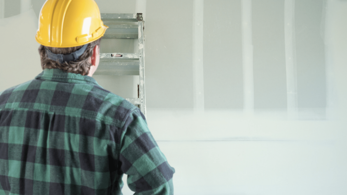 backside of contractor in hardhat staring at drywall